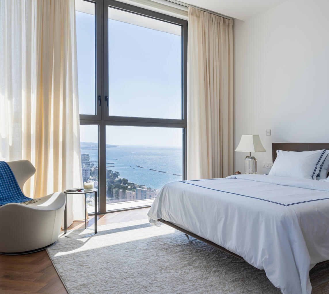 Interior photography of a modern bedroom with floor-to-ceiling windows and panoramic views of Limassol and the Mediterranean Sea.